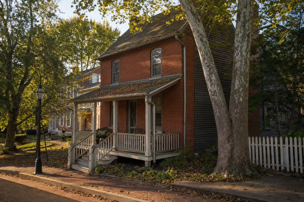 Old two-story red-brick house with a deep porch, half-round gutters and a big sycamore in front