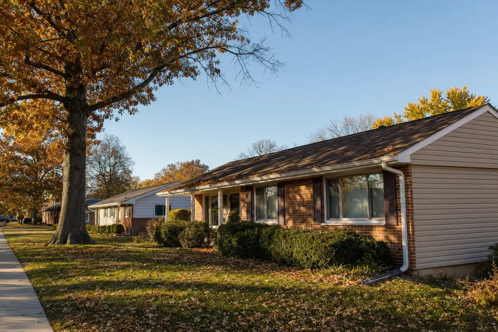 Brick ranch house under a big oak in October, leaves on the lawn and along the gutter line