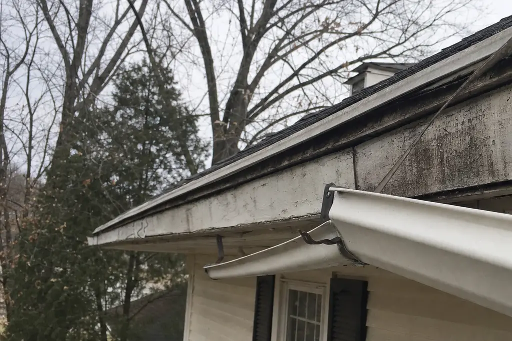 White gutter sagging away from a stained fascia board, one hanger bent and pulled loose